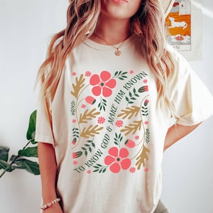 May include: A cream colored t-shirt with a floral design and the text "To Know God & Make Him Known".