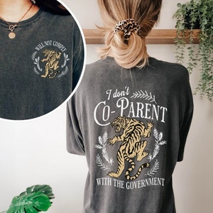 May include: A dark gray t-shirt with a tiger graphic and the text "I don't co-parent with the government".