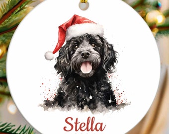 May include: A black dog wearing a red Santa hat with a white trim. The dog is looking at the camera with its tongue sticking out. The dog's name, Stella, and the year 2024 are written in red below the dog. The background is white with red and silver glitter.