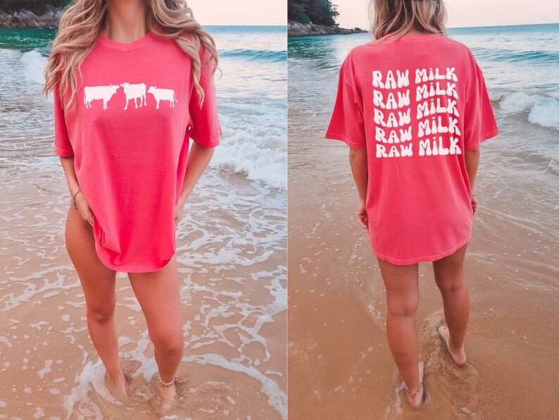 May include: A pink oversized t-shirt with a white graphic of three cows on the front and the text "RAW MILK" repeated five times on the back.