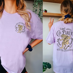 May include: A purple t-shirt with a tiger graphic and the text "Will Not Comply" on the front and the text "I don't Co-Parent with the Government" on the back.