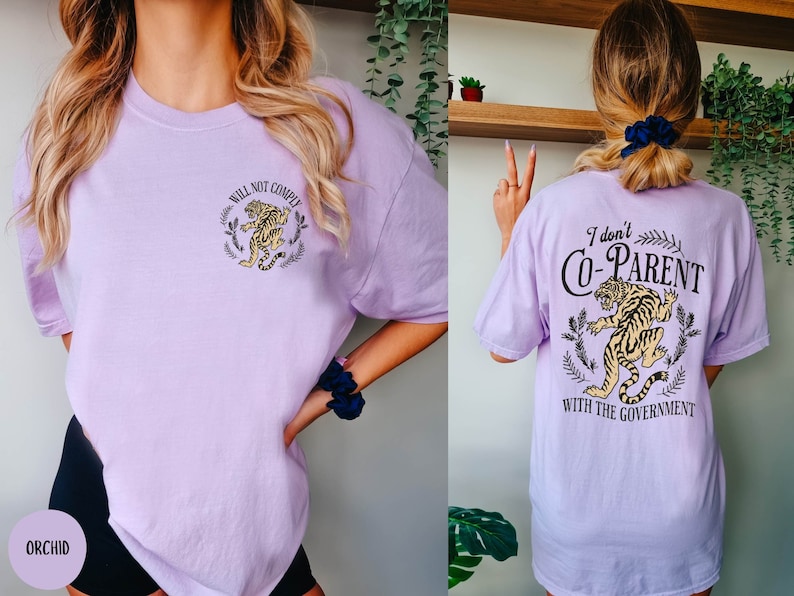 May include: A purple t-shirt with a tiger graphic and the text "Will Not Comply" on the front and the text "I don't Co-Parent with the Government" on the back.