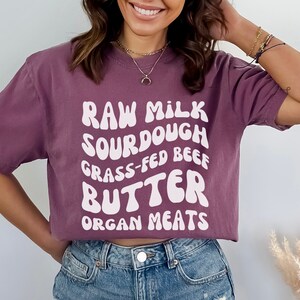 May include: A purple cropped t-shirt with white text that reads "Raw Milk Sourdough Grass-Fed Beef Butter Organ Meats".