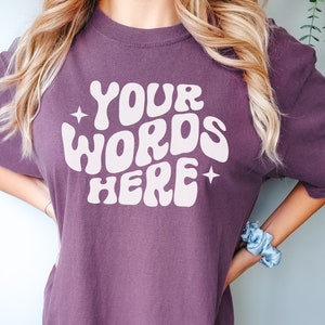May include: A purple t-shirt with the text "YOUR WORDS HERE" in a retro, white font.