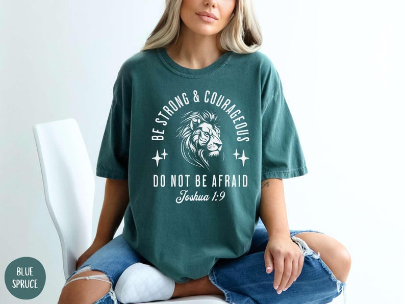 Pu&ograve; includere: Una maglietta blu turchese con una stampa grafica bianca di un leone con il testo "Be Strong & Courageous, Do Not Be Afraid, Joshua 1:9".
