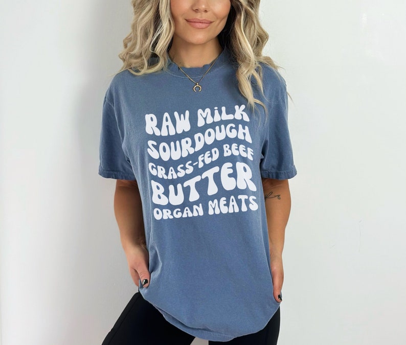 May include: A blue t-shirt with white text that reads "Raw Milk Sourdough Grass-Fed Beef Butter Organ Meats".