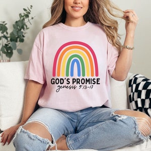 K&ouml;nnte beinhalten: Ein pinkfarbenes T-Shirt mit einem Regenbogen-Motiv und dem Text "GOD'S PROMISE genesis 9:13-17".