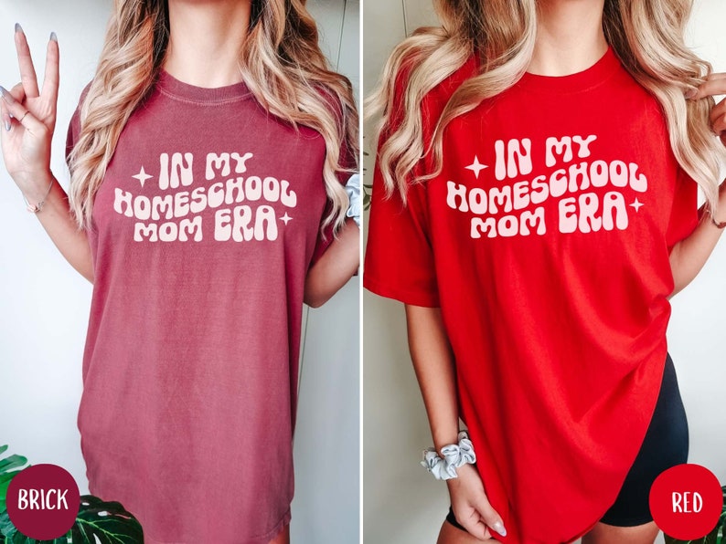 May include: Two women wearing oversized t-shirts with the text "In My Homeschool Mom Era" in a retro font. The shirt on the left is brick red and the shirt on the right is red.