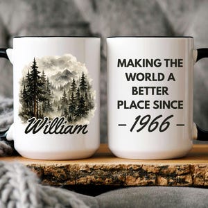 May include: White ceramic mug with a black handle and rim. One side features a forest scene with the name "William". The other side reads "MAKING THE WORLD A BETTER PLACE SINCE - 1966 - ".