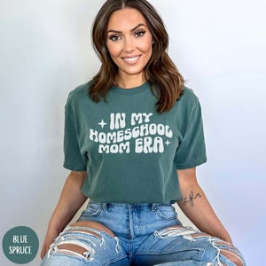 May include: A woman wearing a green t-shirt with the text "In My Homeschool Mom Era" in white. The shirt has a distressed look and the text is in a retro font.