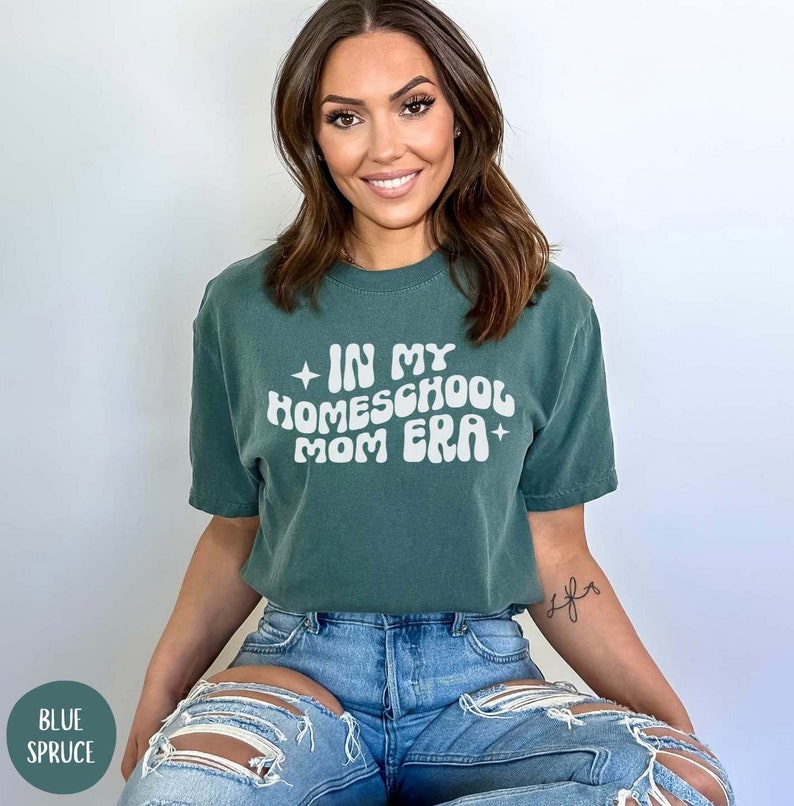 May include: A woman wearing a green t-shirt with the text "In My Homeschool Mom Era" in white. The shirt has a distressed look and the text is in a retro font.