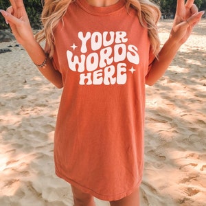 May include: A coral coloured t-shirt with a white graphic that says "YOUR WORDS HERE" in a retro font.
