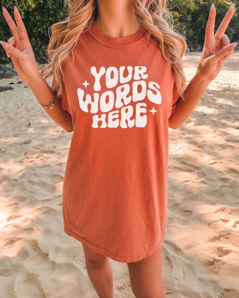 May include: A coral coloured t-shirt with a white graphic that says "YOUR WORDS HERE" in a retro font.