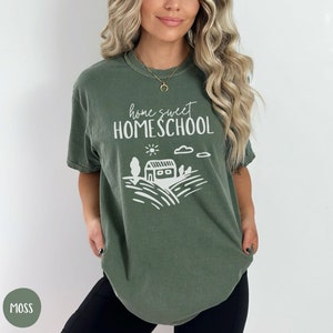 May include: A green t-shirt with the text "home sweet HOMESCHOOL" in white. The shirt also features a white illustration of a house with a sun, clouds, and trees.