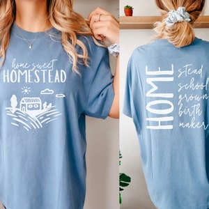 May include: A light blue t-shirt with a white graphic on the front that says "home sweet homestead" and a white graphic on the back that says "HOME stead school grown birth maker".