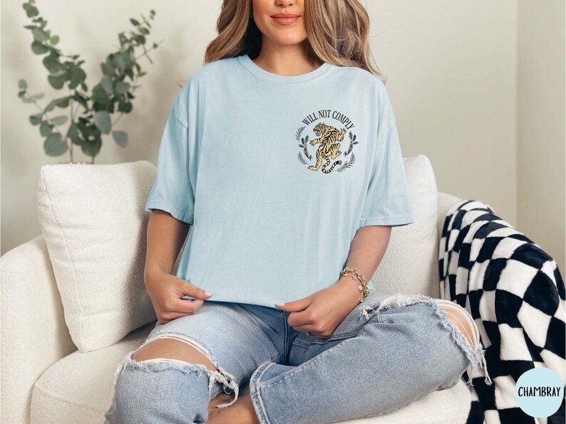 May include: A light blue t-shirt with a graphic of a tiger and the text "Will Not Comply".