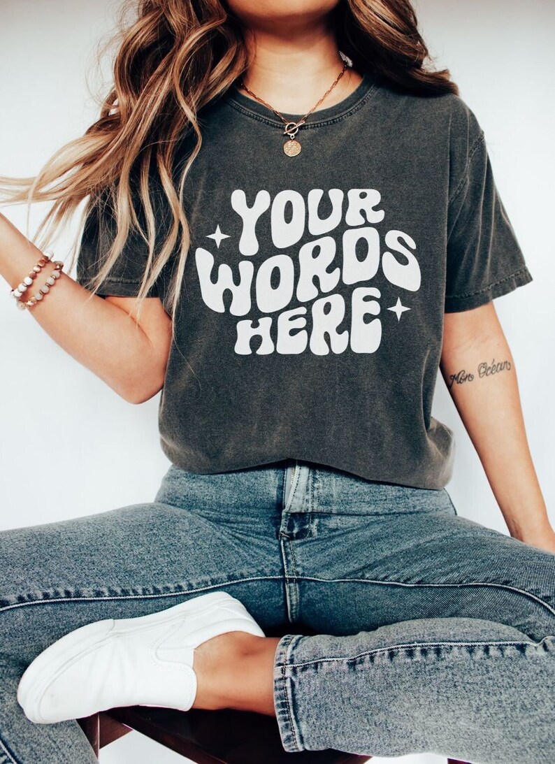 May include: A dark grey t-shirt with a white graphic that says "YOUR WORDS HERE" in a retro font. The shirt has a relaxed fit and is made of a soft, comfortable fabric.