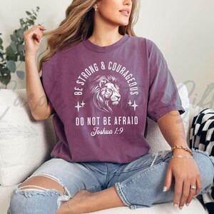 Pu&ograve; includere: Una maglietta viola con un leone bianco e il testo "Be Strong & Courageous, Do Not Be Afraid, Joshua 1:9".