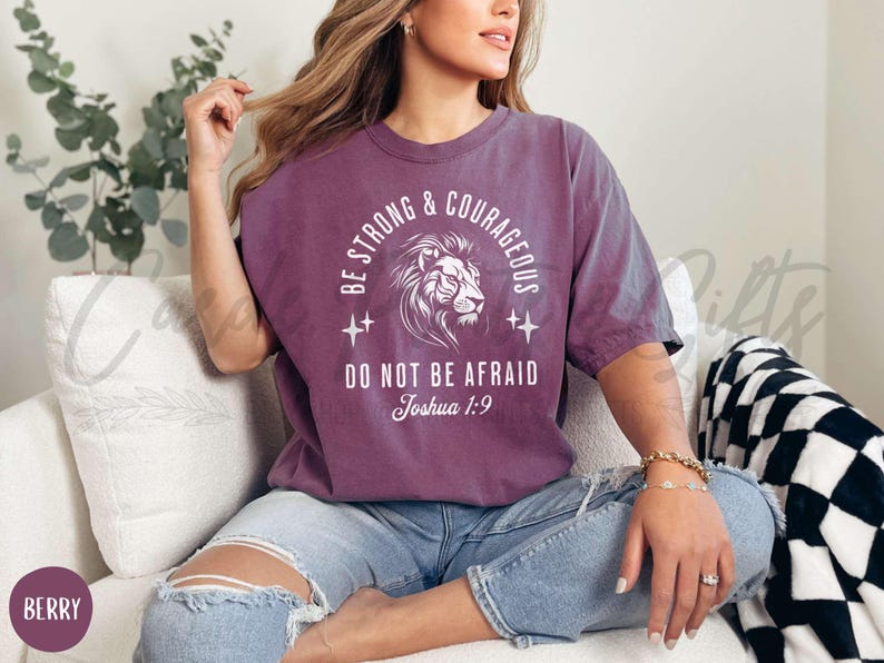 Pu&ograve; includere: Una maglietta viola con un leone bianco e il testo "Be Strong & Courageous, Do Not Be Afraid, Joshua 1:9".