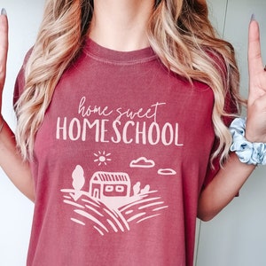 May include: A maroon t-shirt with the text "home sweet HOMESCHOOL" in white. The shirt features a simple illustration of a house with a sun and clouds.