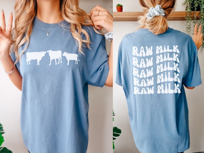 May include: A light blue t-shirt with a white graphic of three cows on the front and the text "RAW MILK" repeated five times on the back.