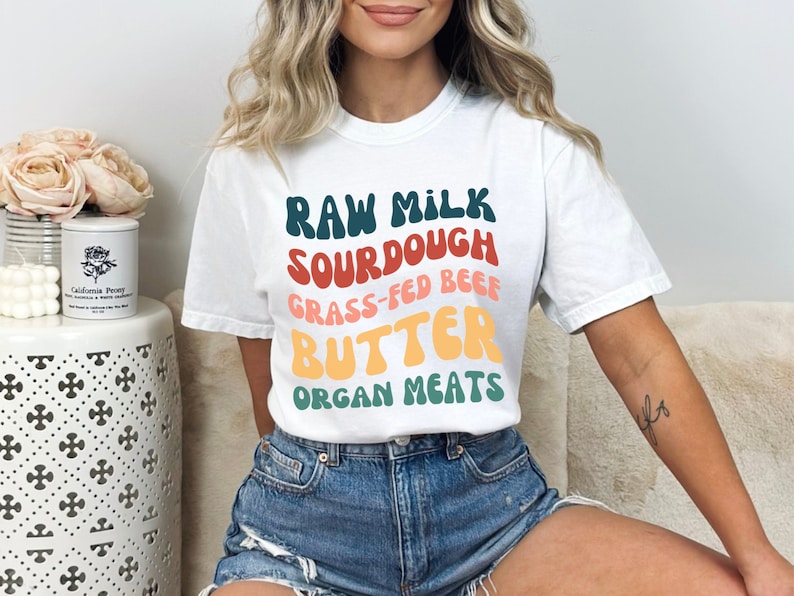 May include: White t-shirt with a colorful graphic that says "Raw Milk Sourdough Grass-Fed Beef Butter Organ Meats".