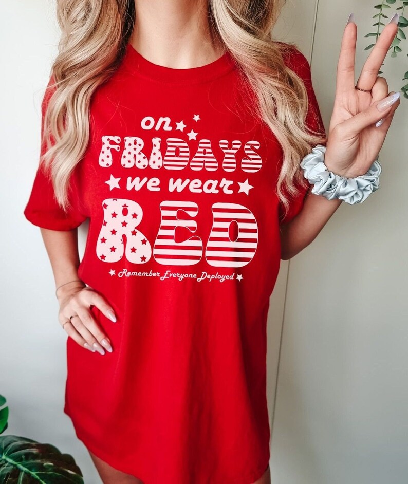 Peut inclure: T-shirt rouge avec un motif blanc qui dit "on Fridays we wear red" avec des &eacute;toiles et des rayures. Le texte "Remember Everyone Deployed" est sous le motif.