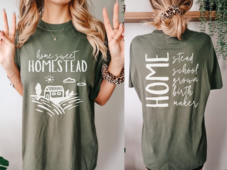 May include: A green t-shirt with the text "home sweet homestead" on the front and a stylized illustration of a house and fields. The back of the shirt has the word "HOME" vertically down the left side and the words "stead, school, grown, birth, maker" vertically down the right side.