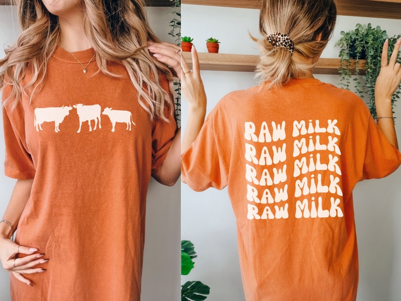 May include: Orange t-shirt with a white silhouette of three cows on the front and the text "RAW MILK" repeated five times in a retro font on the back.