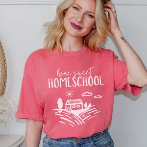 May include: A pink t-shirt with the text "home sweet homeschool" and a white illustration of a house, sun, and clouds.