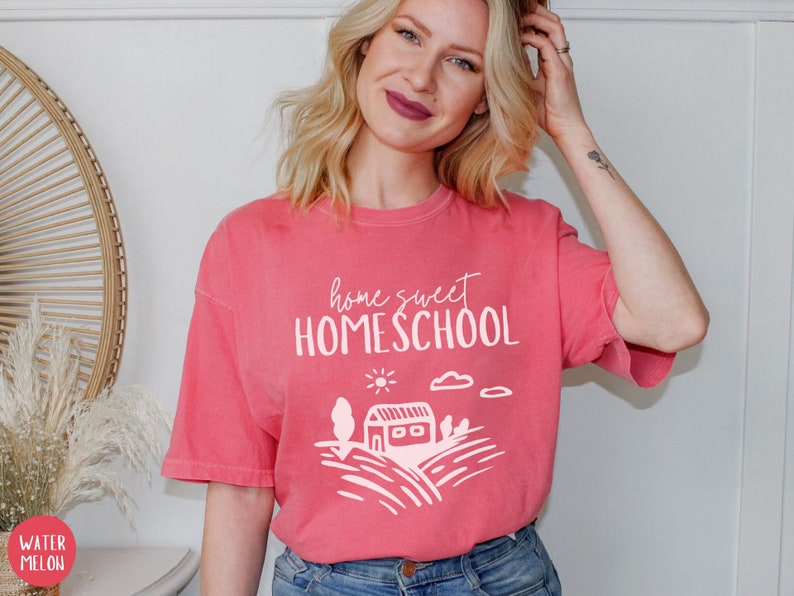 May include: A pink t-shirt with the text "home sweet homeschool" and a white illustration of a house, sun, and clouds.