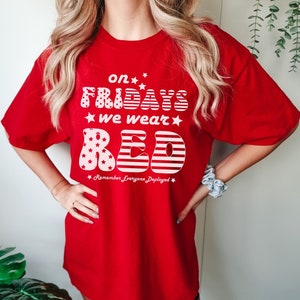 Peut inclure: T-shirt rouge avec un motif blanc qui dit "On Fridays we wear red" avec des &eacute;toiles et un design de drapeau am&eacute;ricain. Le texte "Remember Everyone Deployed" est sous le graphique.