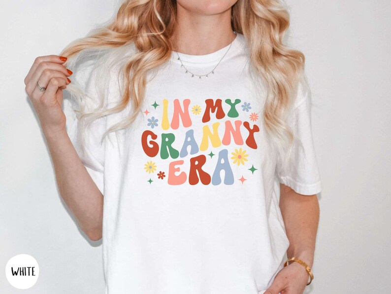 May include: White t-shirt with the text "In My Granny Era" in colorful retro font with flowers and stars.
