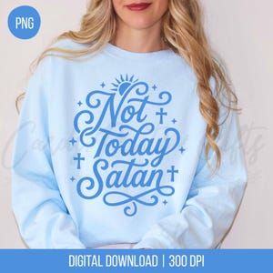 May include: Light blue sweatshirt with the phrase "Not Today Satan" in a stylized blue font. The design includes crosses, stars, and a sun. The words "DIGITAL DOWNLOAD | 300 DPI" are at the bottom.