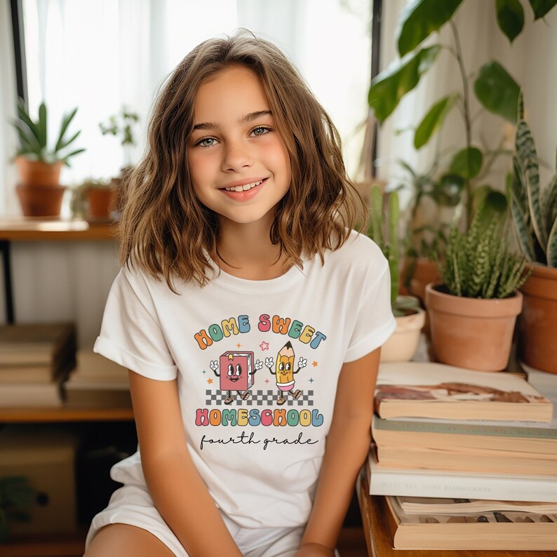 May include: A white t-shirt with a colorful graphic design that says "Home Sweet Homeschool fourth grade". The graphic features a cartoon book and pencil holding hands.