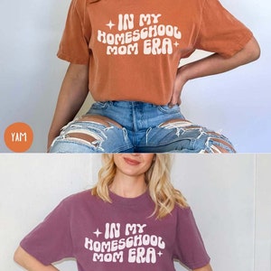 May include: Two t-shirts with the text "In My Homeschool Mom Era" in a retro font. The top shirt is rust orange and the bottom shirt is a deep purple.