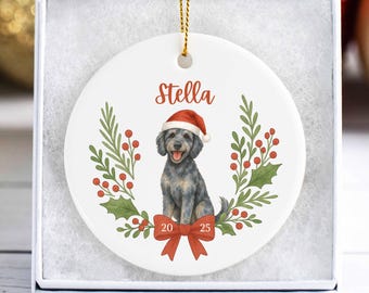 May include: White ceramic Christmas ornament featuring a watercolor illustration of a dog wearing a Santa hat. The dog is surrounded by a green and red wreath with the name "Stella" above and the numbers "20 25" below.