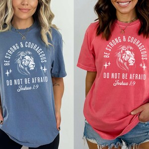 Pu&ograve; includere: Una maglietta blu e una rossa con una stampa grafica bianca di un leone con il testo "Be Strong & Courageous Do Not Be Afraid Joshua 1:9".