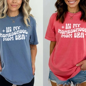May include: Two women wearing t-shirts with the text "In My Homeschool Mom Era" in a retro font. The shirt on the left is blue and the shirt on the right is pink.
