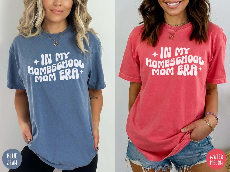May include: Two women wearing t-shirts with the text "In My Homeschool Mom Era" in a retro font. The shirt on the left is blue and the shirt on the right is pink.