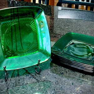 Peut inclure: Un ensemble de six assiettes carrées en verre vert avec un motif en relief autour du bord. Les assiettes sont empilées les unes sur les autres.