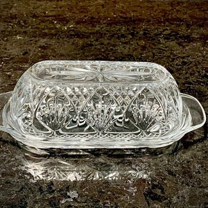 May include: A clear glass butter dish with a decorative, cut-glass design. The dish has a lid and a base.