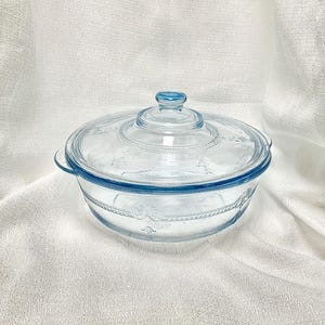 May include: A clear glass baking dish with a lid. The dish has a blue rim and a floral design. The lid is also clear glass with a blue rim.