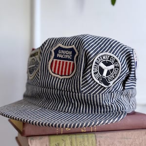 May include: A blue and white striped railroad engineer's cap with patches that say "Union Pacific" and "The Belt Railway Co. of Chicago".