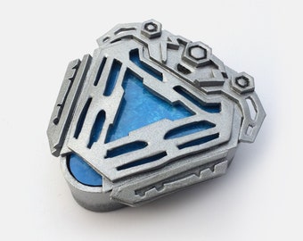 May include: A silver and blue 3D printed replica of the Arc Reactor from the Marvel Cinematic Universe. The reactor is a triangular shape with a blue glowing core.