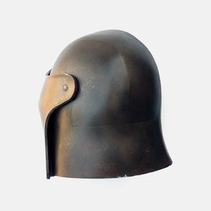 May include: A dark brown helmet with a gold-coloured visor. The helmet has a rounded top and a slightly pointed chin guard.