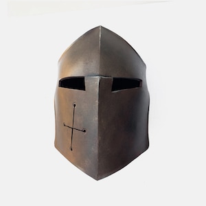 May include: A brown metal helmet with a cross design and eye slits. The helmet is made of textured metal and has a slightly weathered look.