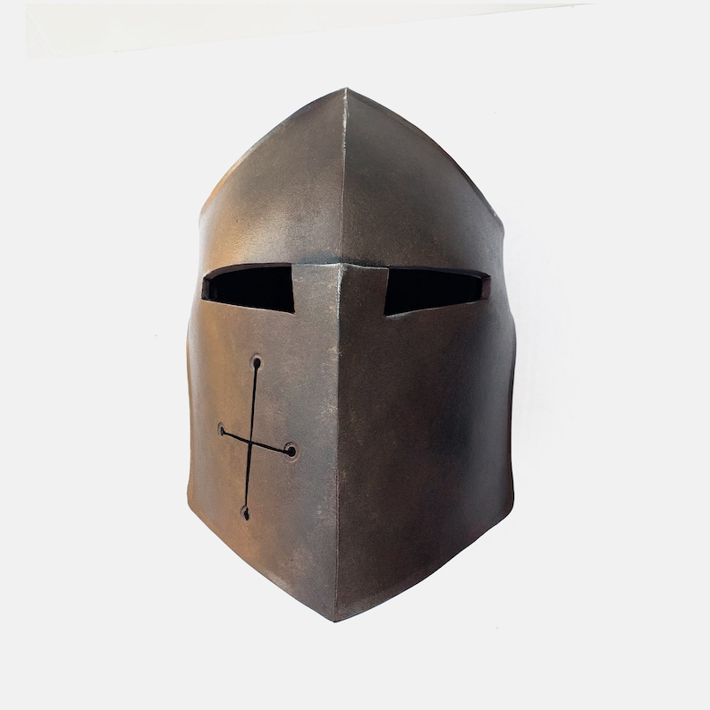 May include: A brown metal helmet with a cross design and eye slits. The helmet is made of textured metal and has a slightly weathered look.