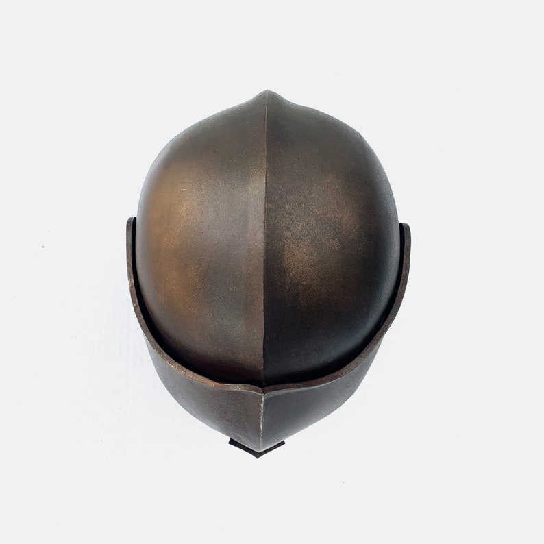 May include: A bronze helmet with a rounded top and a curved brim. The helmet is made of a smooth, metallic material.