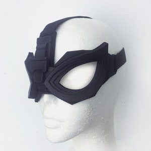 May include: A black eye mask with a geometric design. The mask has a strap that goes around the head.